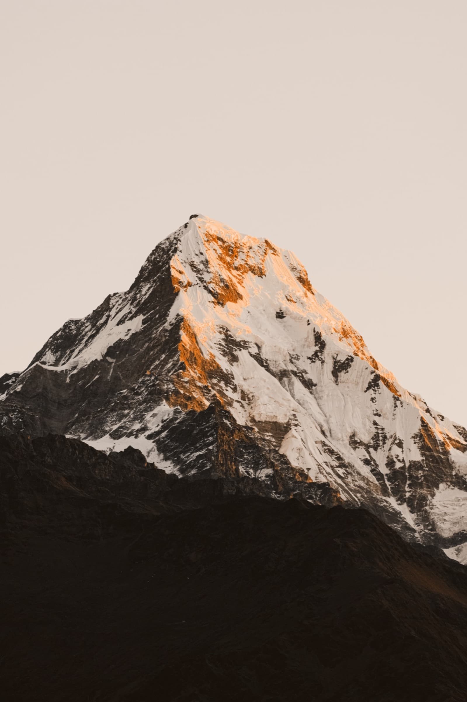 A snow-capped peak, its summit ridge lit copper by first light